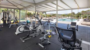 A covered gym area with exercise equipment, a pool, and outdoor seating.
