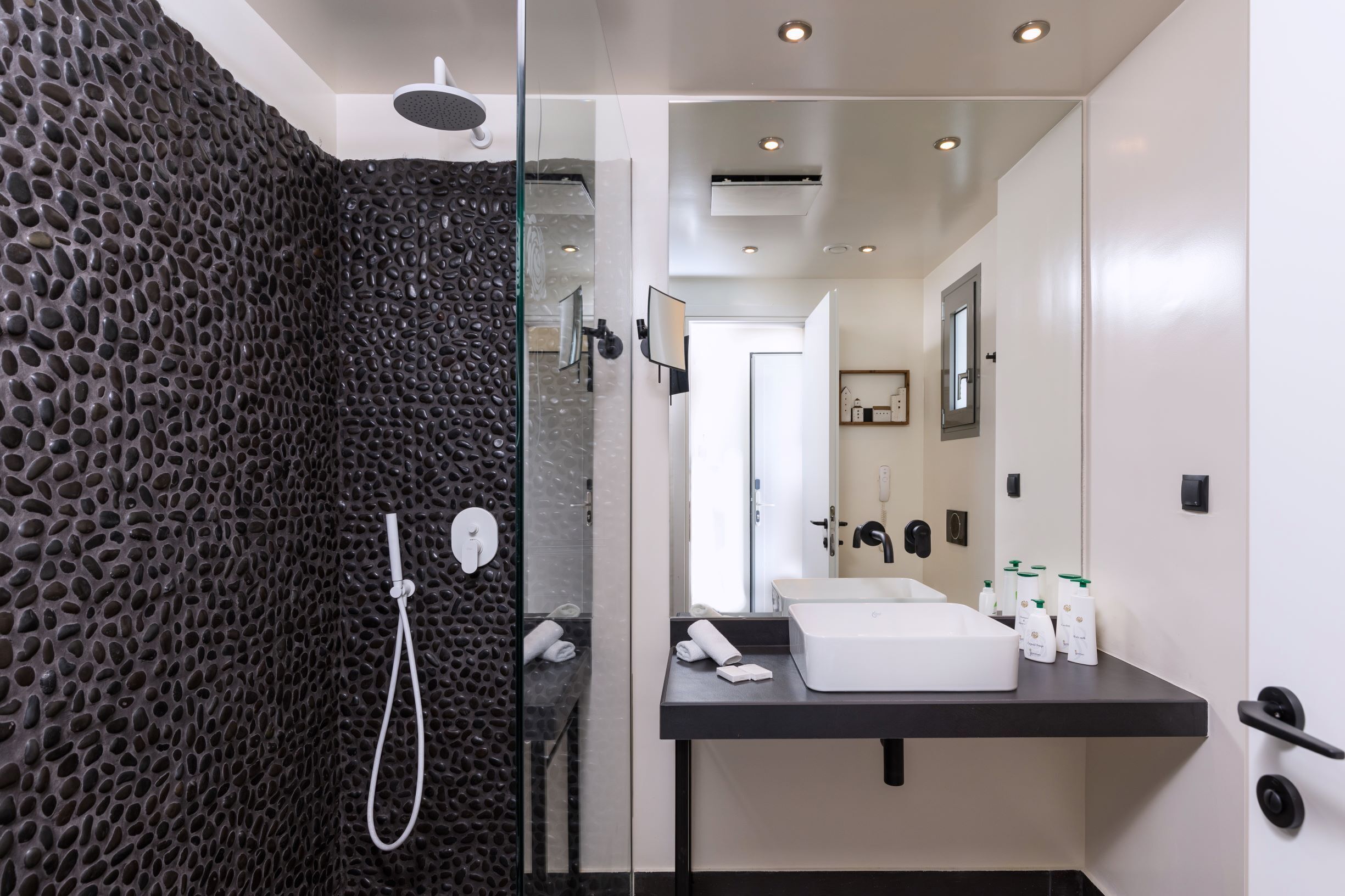 A modern bathroom with a glass-enclosed shower, a white sink, and toiletries on the counter.