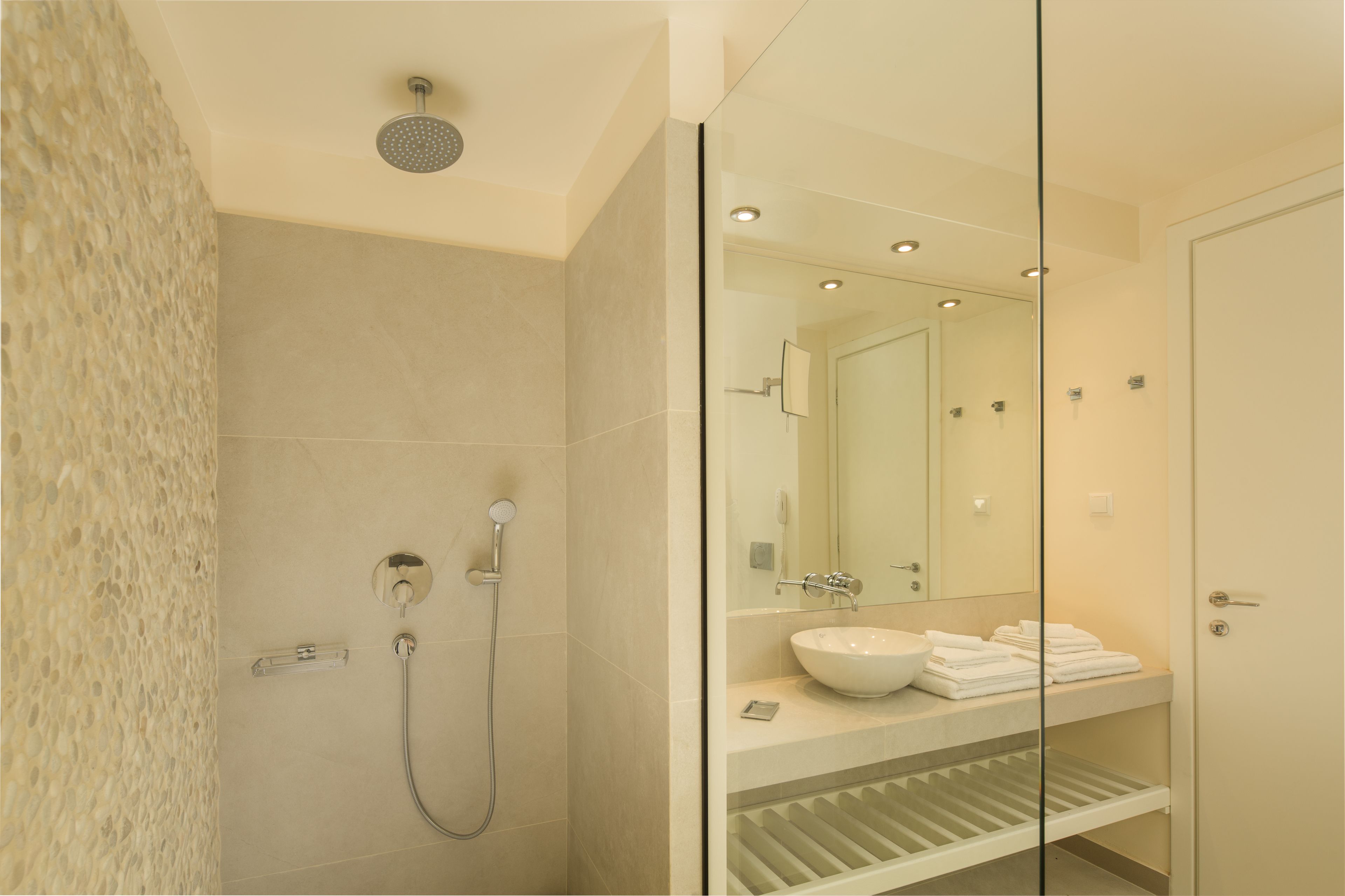 Un bagno moderno con cabina doccia in vetro, uno specchio grande e un lavandino bianco.