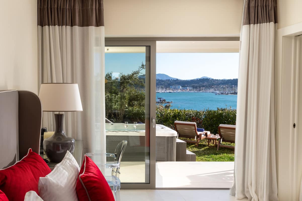 A hotel room with a bed, a desk, a lamp, and a view of a beach and sea.