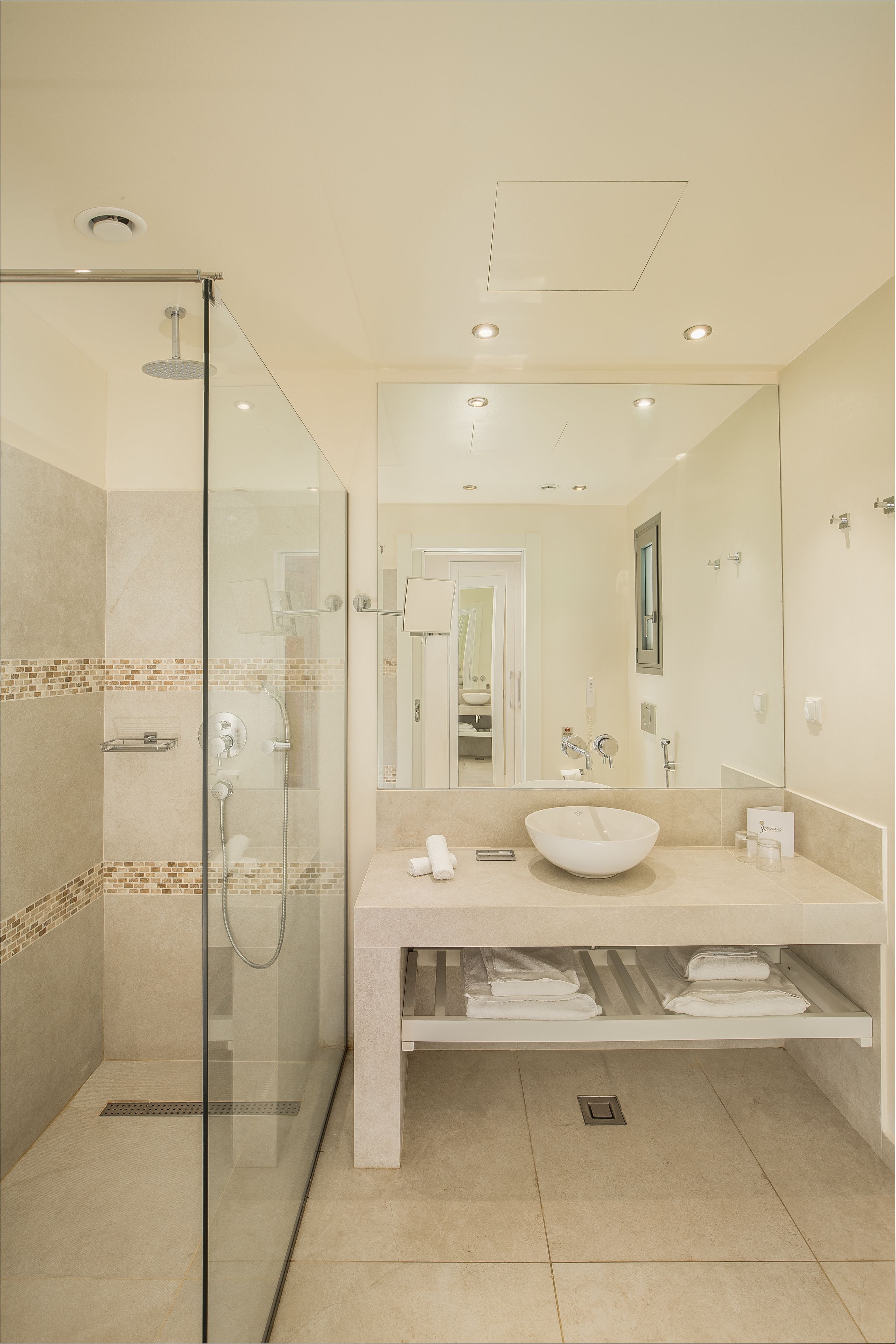 A modern bathroom with a glass-enclosed shower, a large mirror, and a white sink.