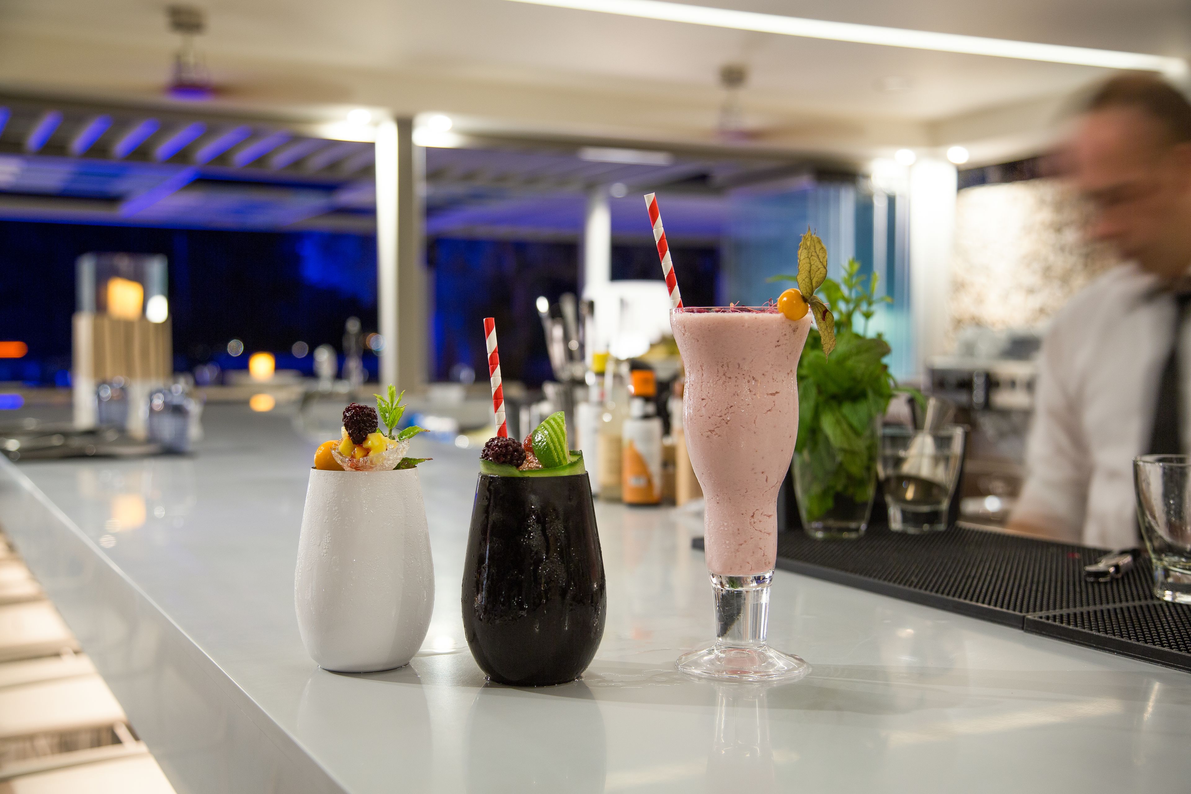 A bar area with three drinks on the counter, a barista in the background, and a modern interior design.