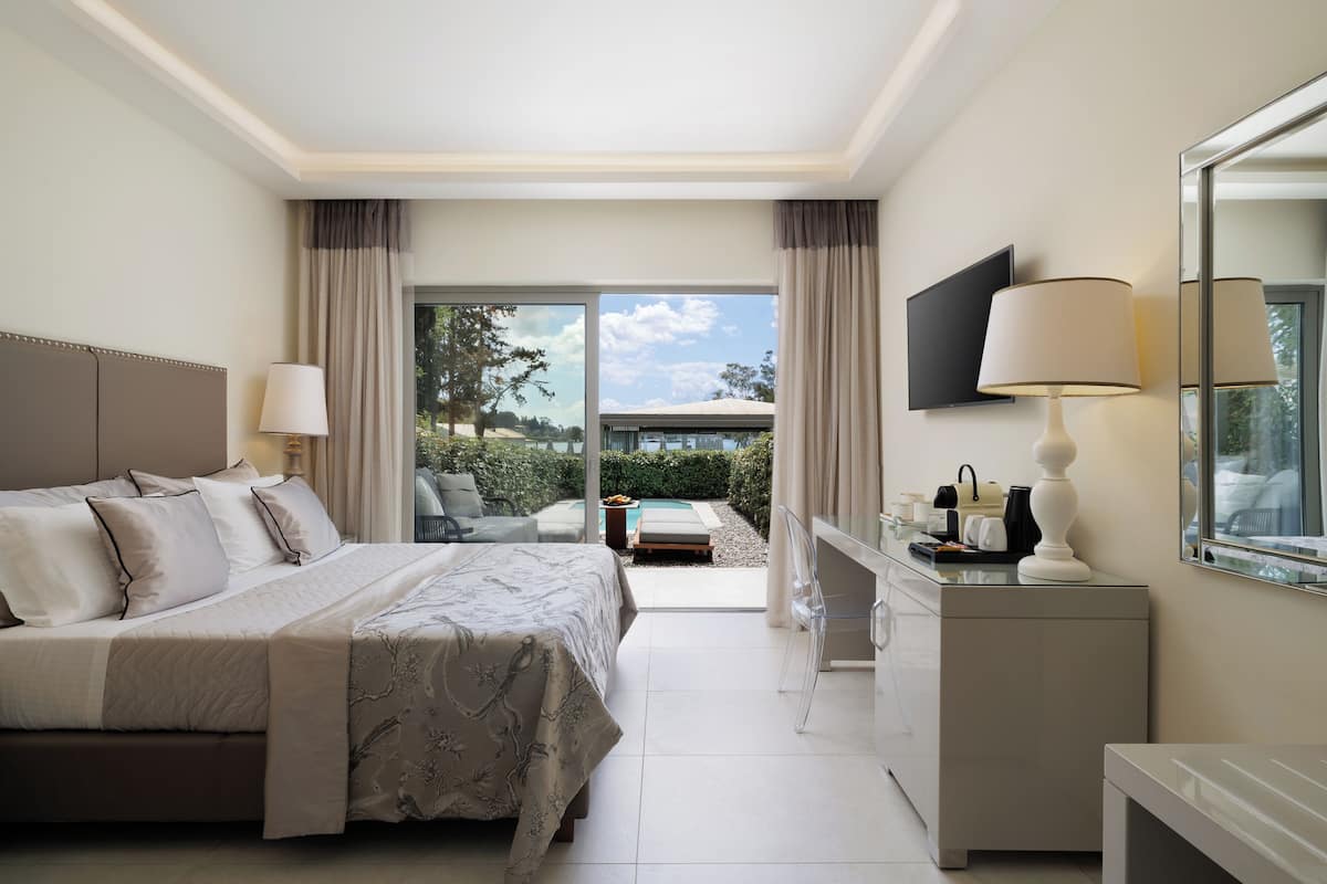 A hotel room with a bed, a desk, a chair, a TV, and a view of the outdoors.