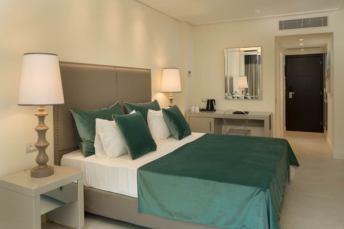 A hotel room with a bed, bedside tables, a desk, a mirror, and a door.