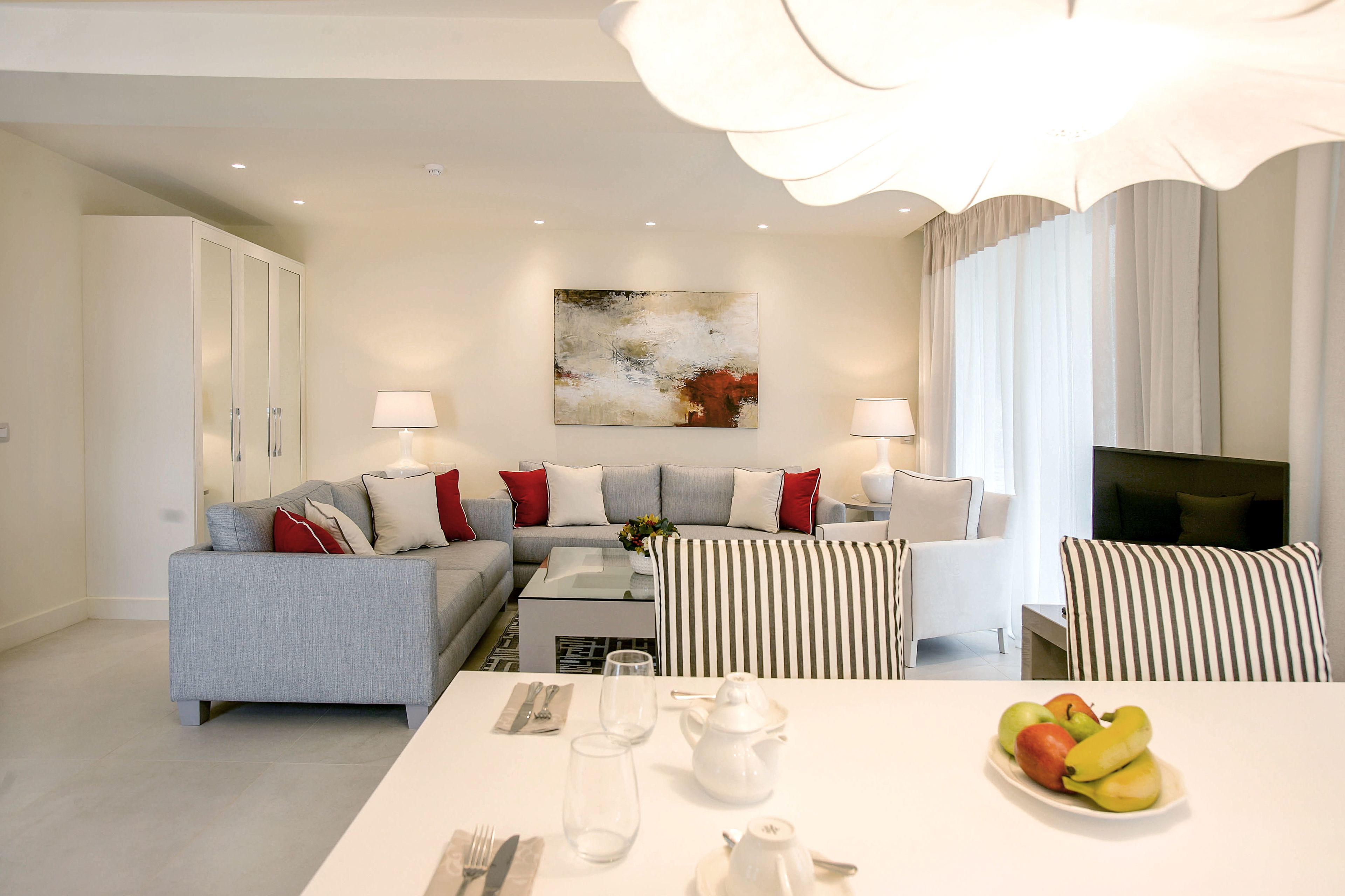 Una sala de estar moderna con un sofá gris, sillones a rayas, una mesa de comedor con vajilla blanca y un frutero.