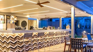 Uma área de bar moderna com parede em padrão ziguezague, um ventilador de teto e vista para o exterior.