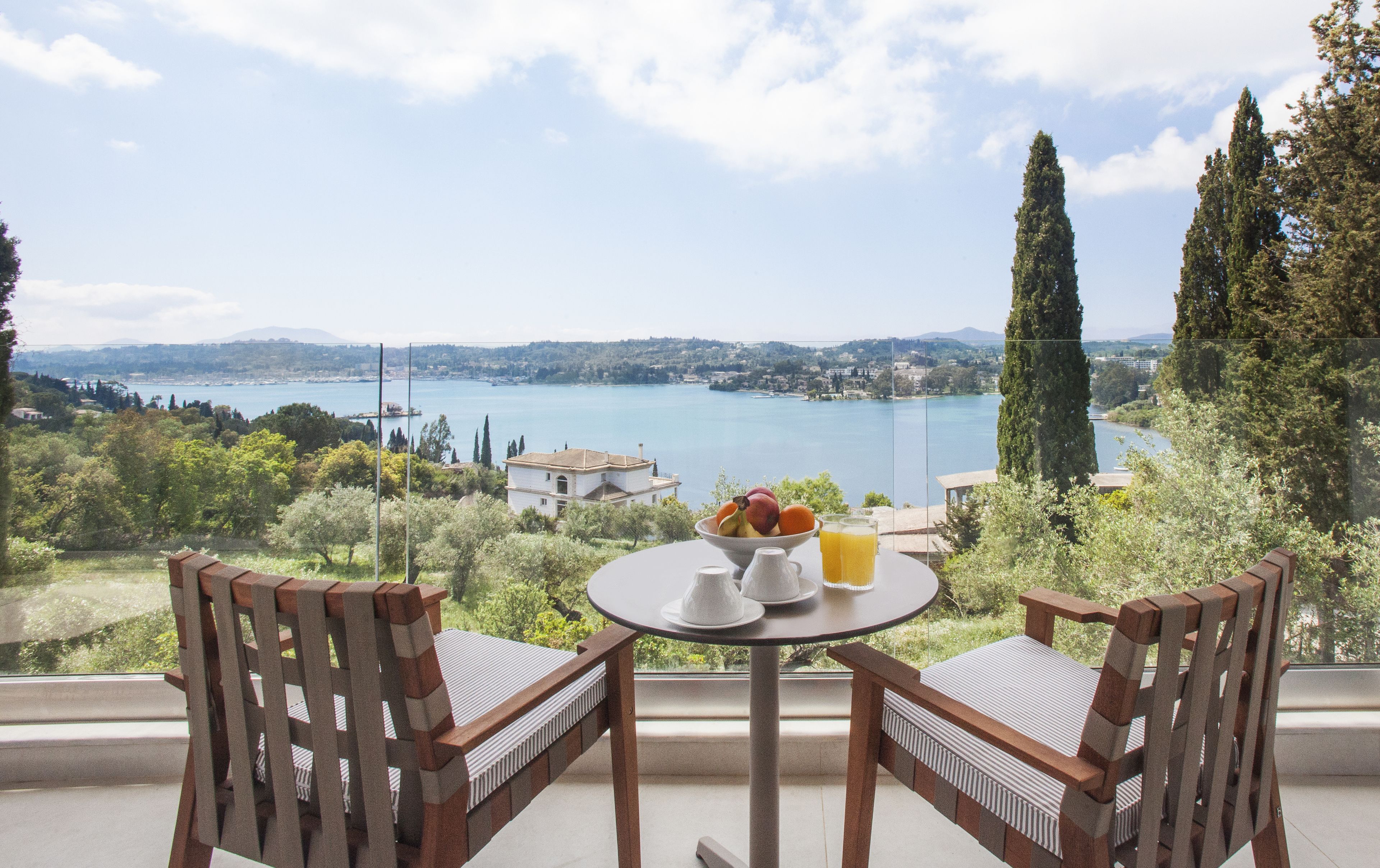 A table with chairs overlooking a lake, a bowl of fruit, and a glass of orange juice.