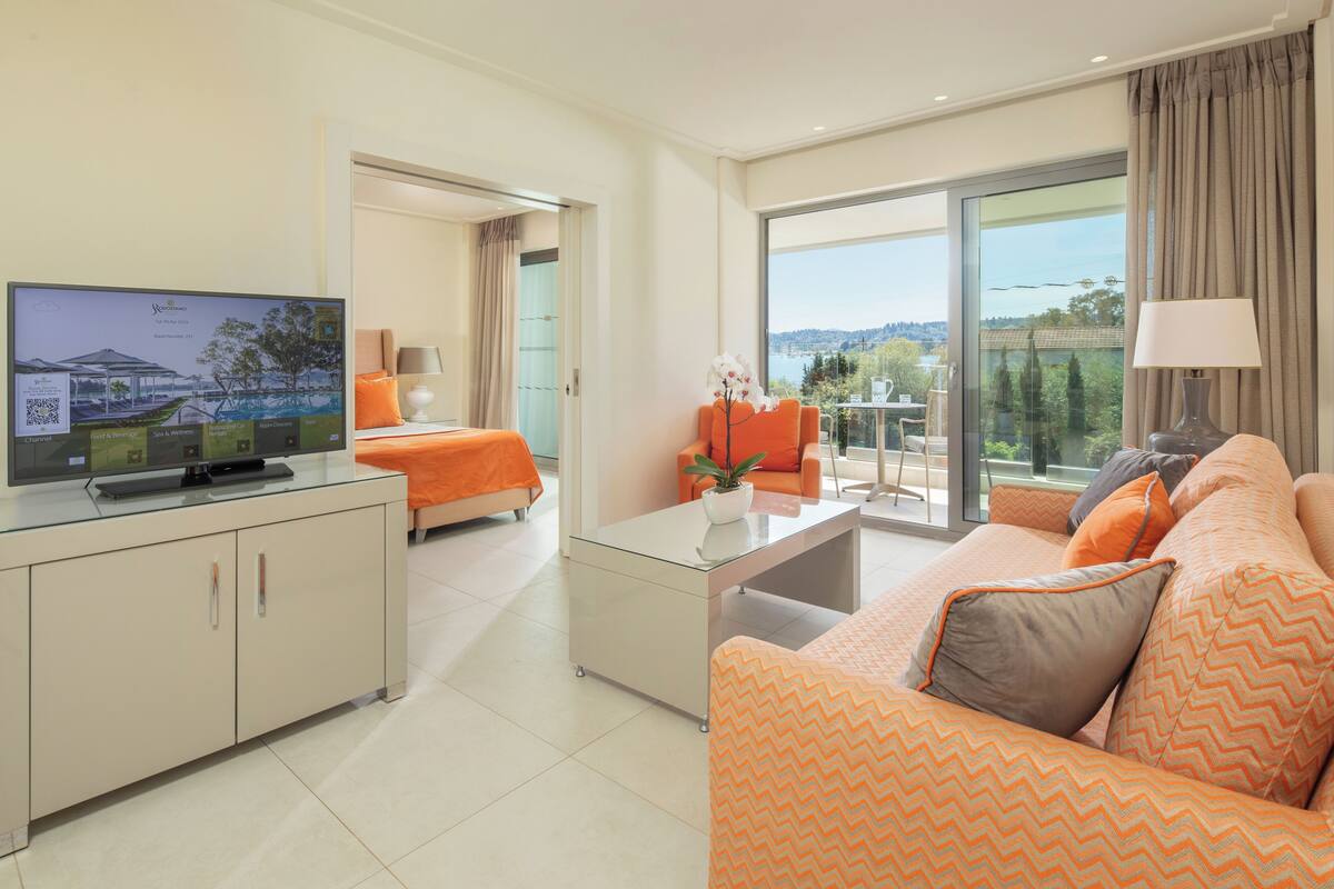 A modern hotel room with a television, orange sofa, and a balcony with a view.