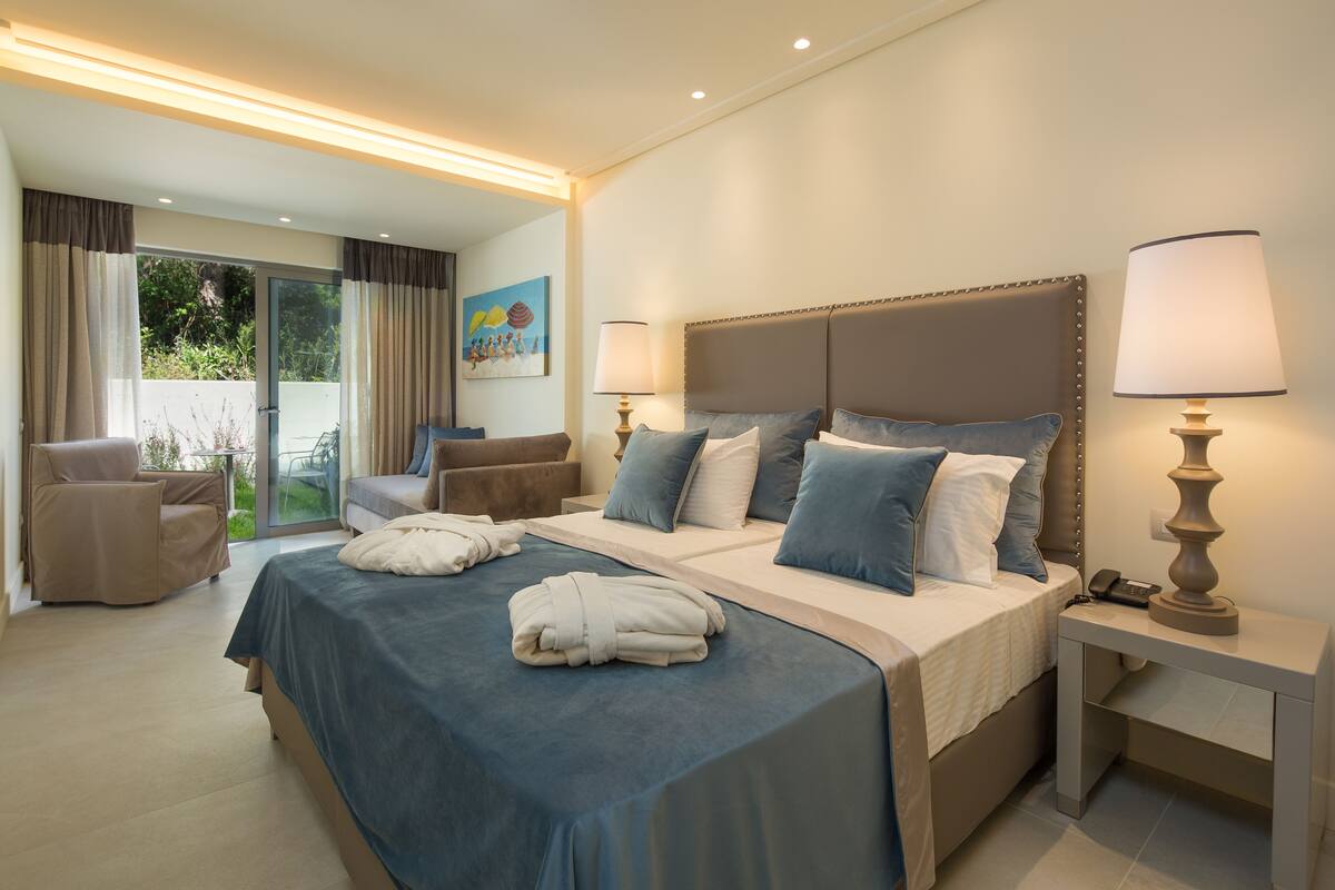 A modern hotel room with a large bed, two bedside tables, a chair, and a view of the outdoors.