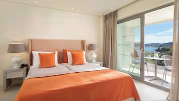 Ein Hotelzimmer mit einem großen Bett, zwei Nachttischen, einem Balkon mit Tisch und Stühlen und Blick aufs Meer.