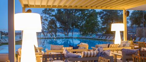 A poolside seating area with tables and chairs, overlooking a swimming pool and trees.