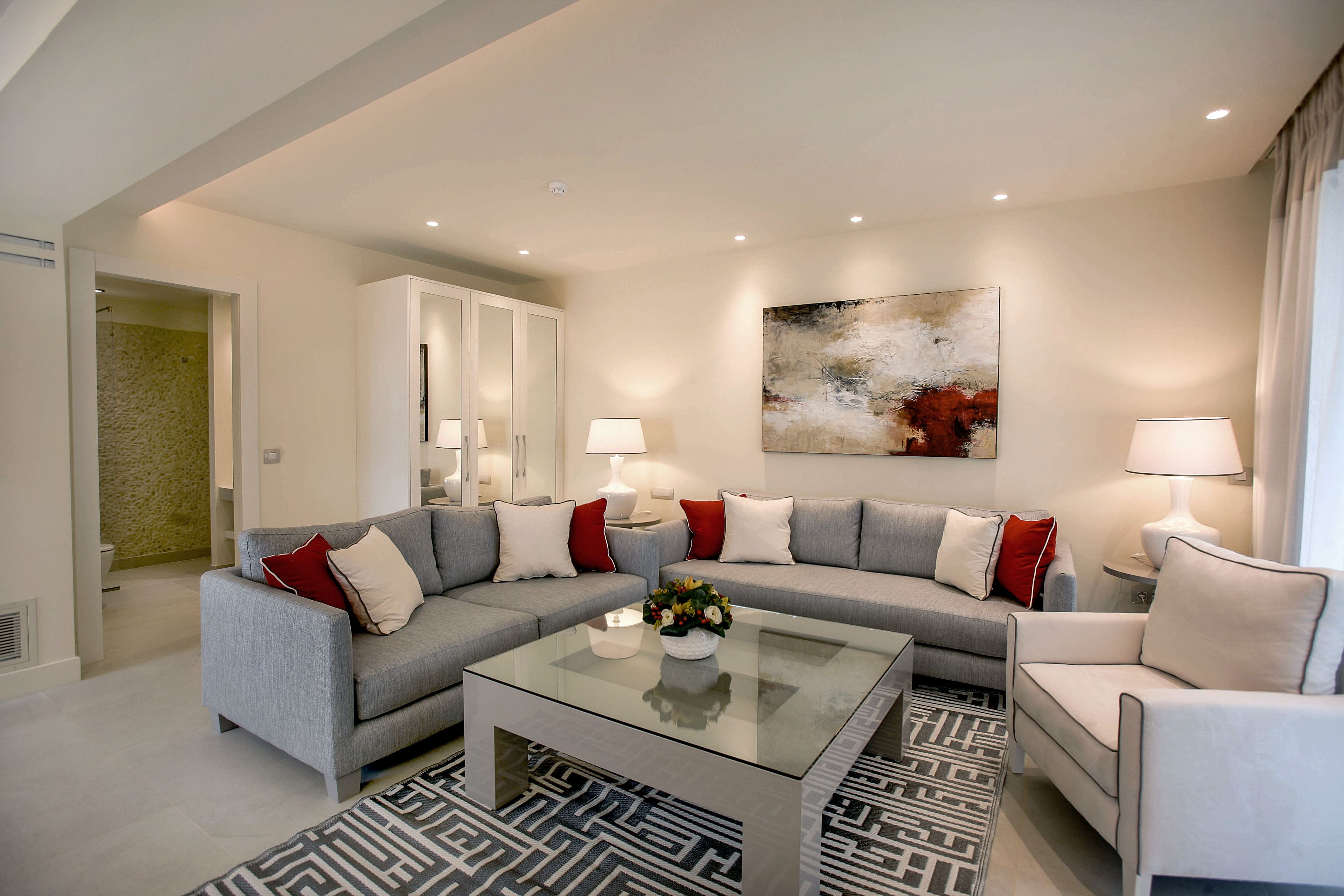 Ein modernes Wohnzimmer mit einem Ecksofa, einem Glastisch und einem gemusterten Teppich.