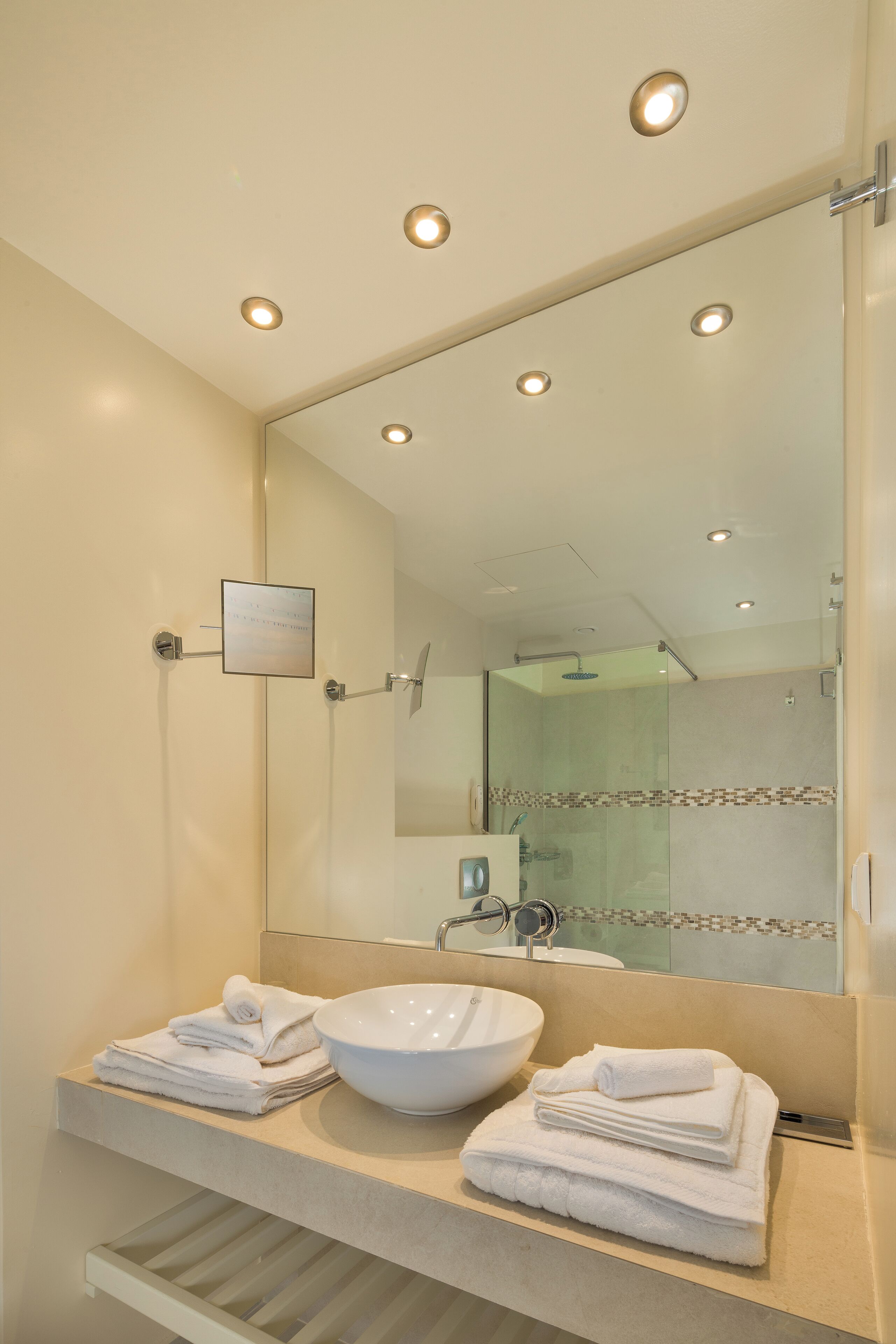 A modern bathroom with a large mirror, a white sink, and a glass shower enclosure.