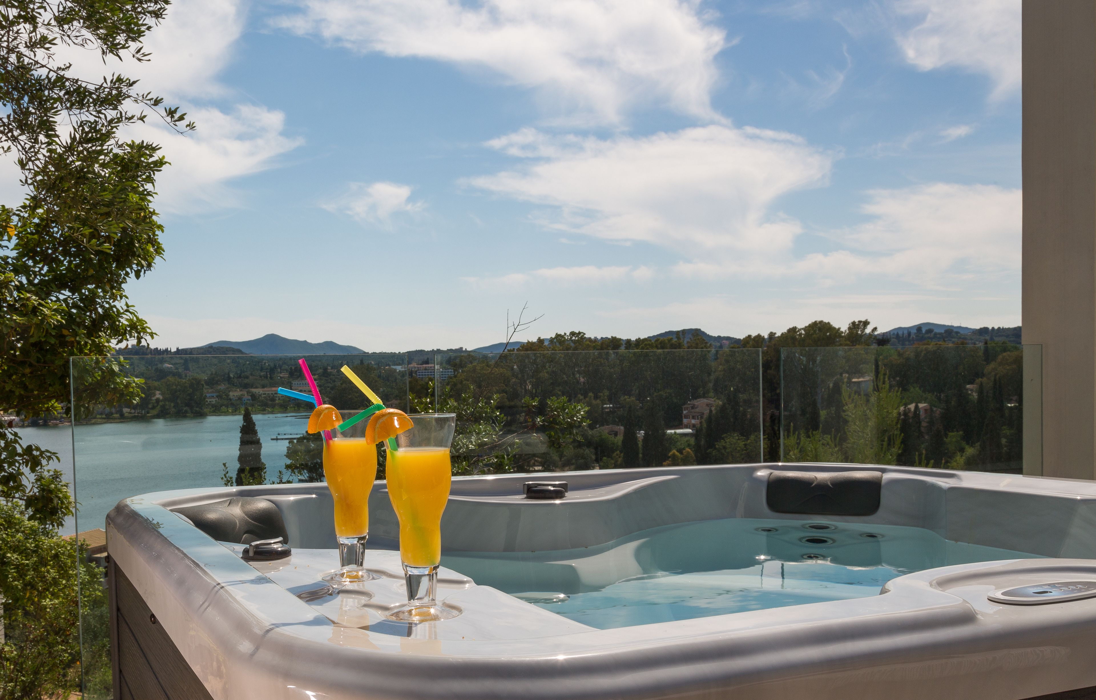 Un jacuzzi con dos bebidas, una vista panorámica de un lago y montañas, y cielo despejado.