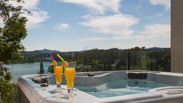 Un jacuzzi con dos bebidas, una vista panorámica de un lago y montañas, y cielo despejado.
