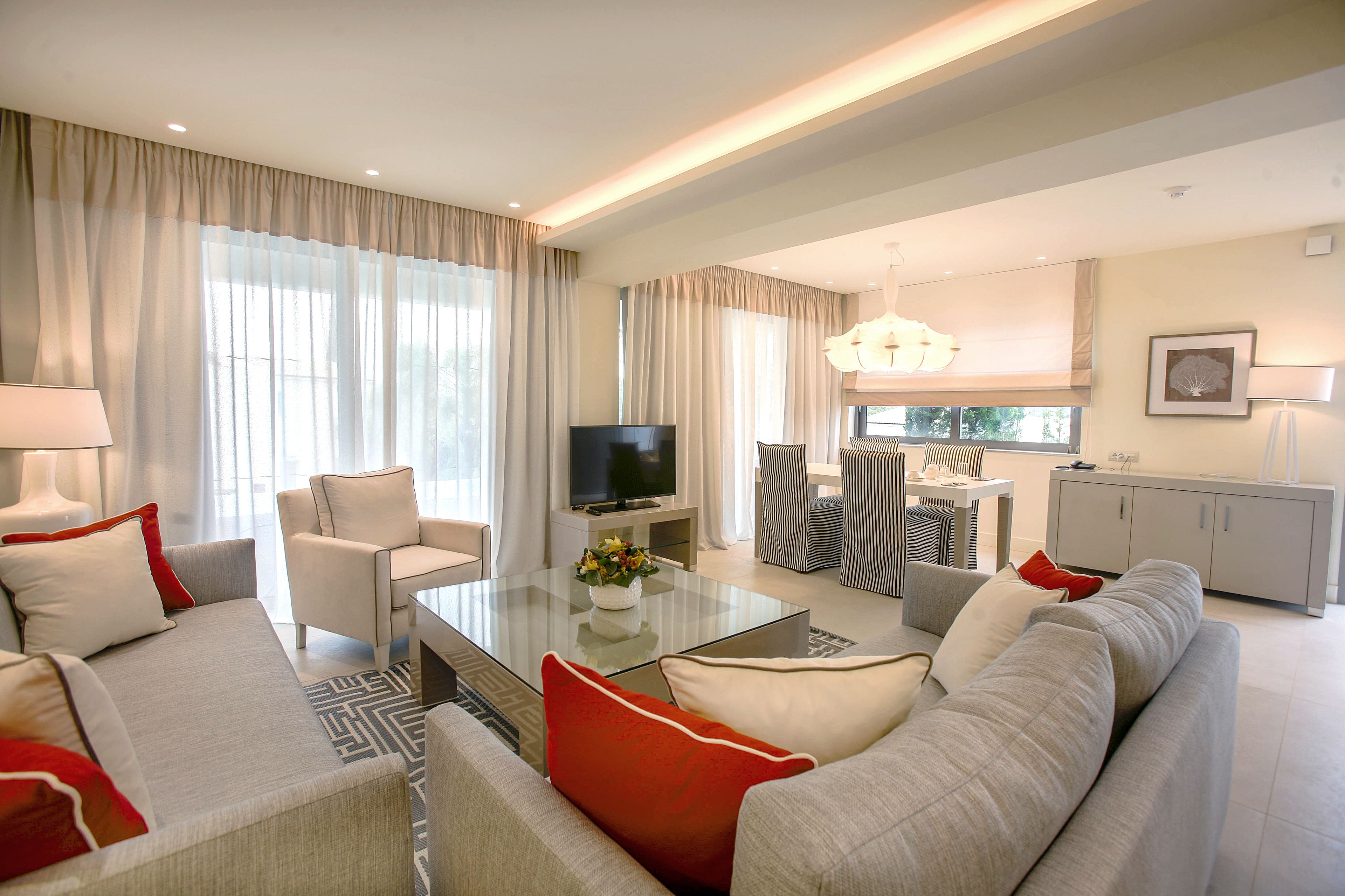 Ein modernes Wohnzimmer mit einer Couch, Sesseln, einem Couchtisch und einem Fernseher.