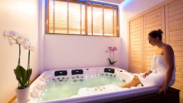 Un cuarto de spa con una bañera grande, paredes de madera y dos orquídeas en macetas.