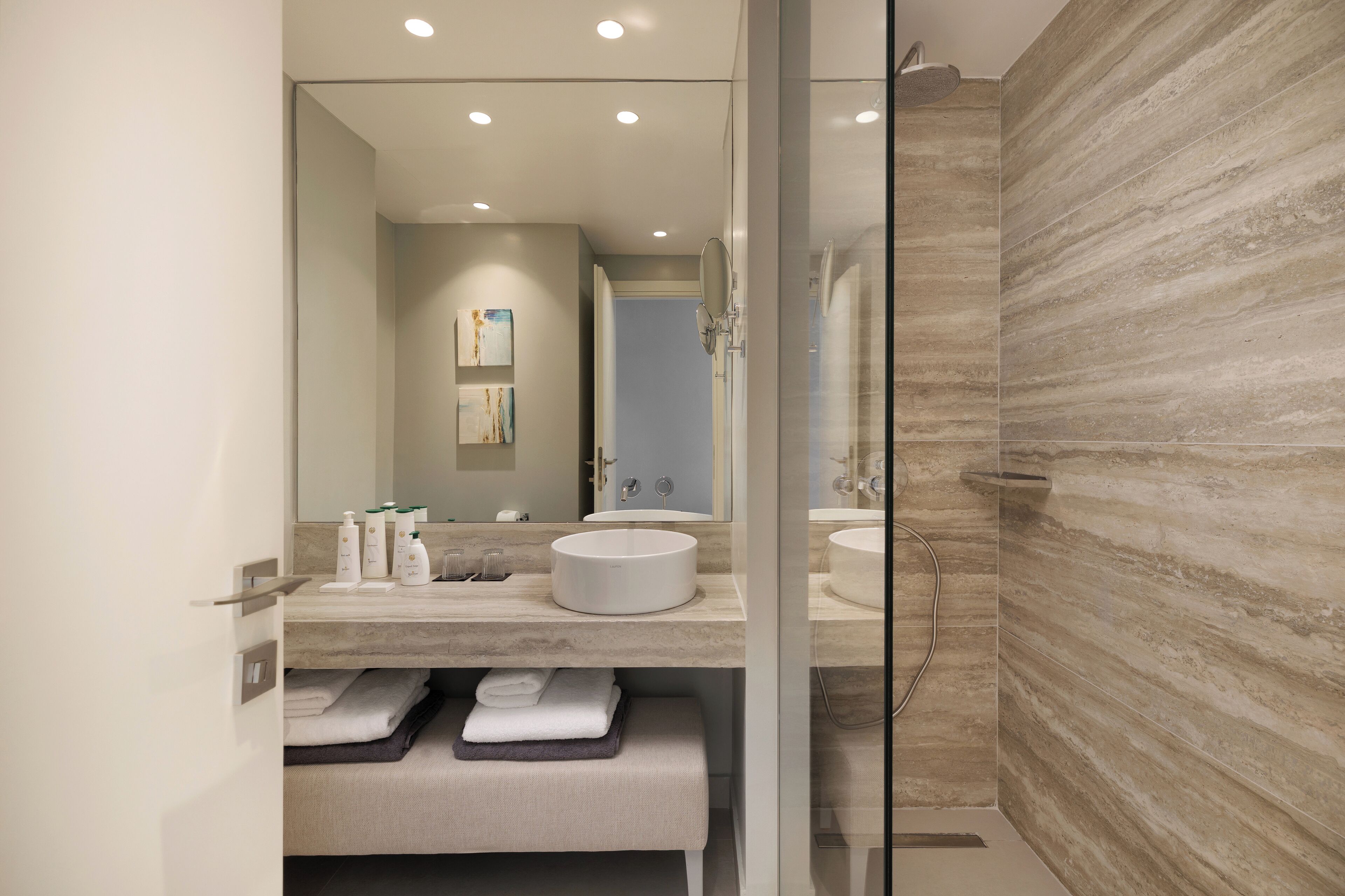 Un baño moderno con un espejo grande, un lavamanos redondo y una cabina de ducha de vidrio.