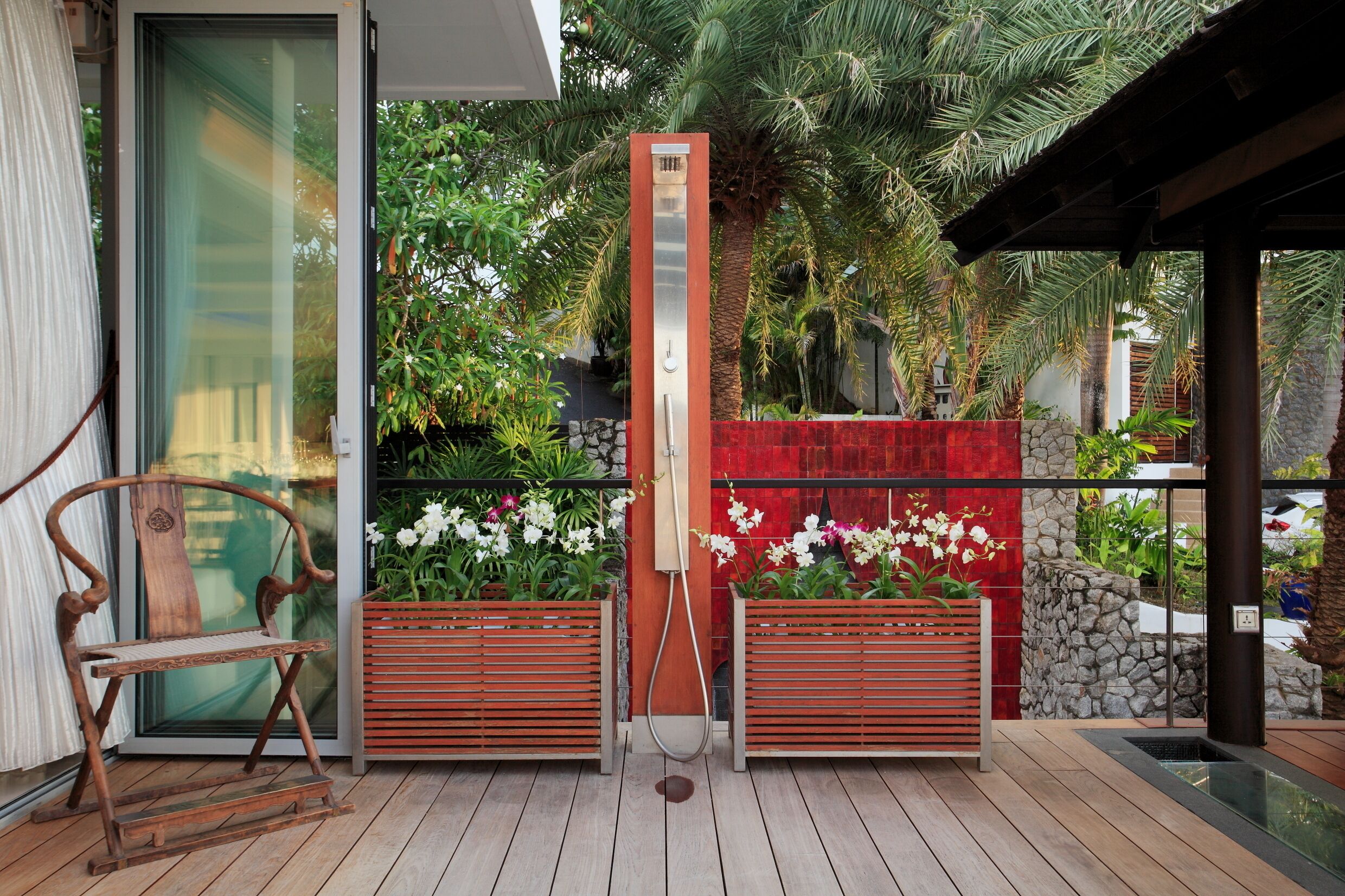 A wooden deck with a built-in bench, a vertical water feature, and lush tropical plants.