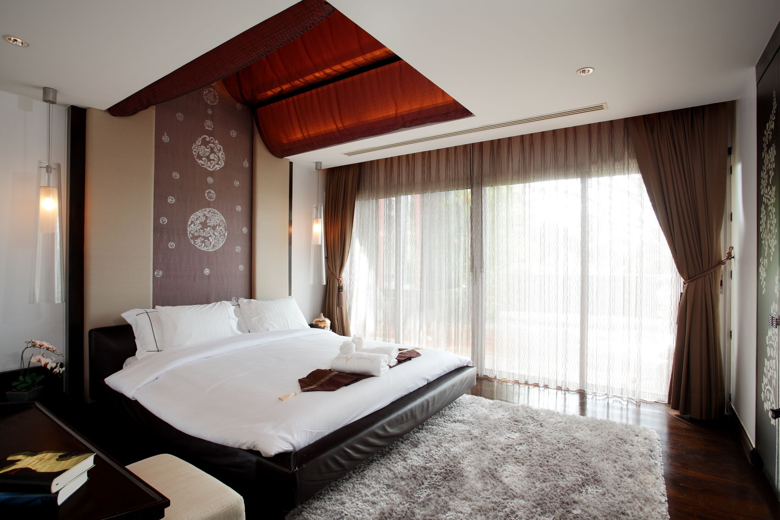 A spacious bedroom with a large bed, a wooden ceiling, and a view of the outdoors through sheer curtains.