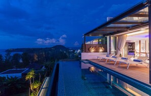 Un área de piscina moderna al aire libre con sillones de descanso y una terraza cubierta de vidrio con vistas panorámicas.