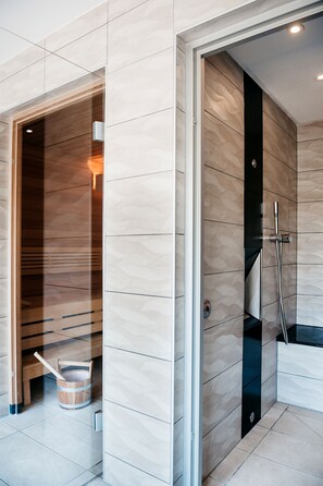 A modern bathroom with a wooden sauna, a glass shower enclosure, and a wooden bucket on the floor. - Logis Hôtel Au Lion Rouge (Bartenheim)