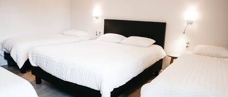 Habitación de hotel con tres camas, cada una con ropa de cama blanca y cabeceros negros. Hay luminarias empotradas en la pared a ambos lados de las camas.