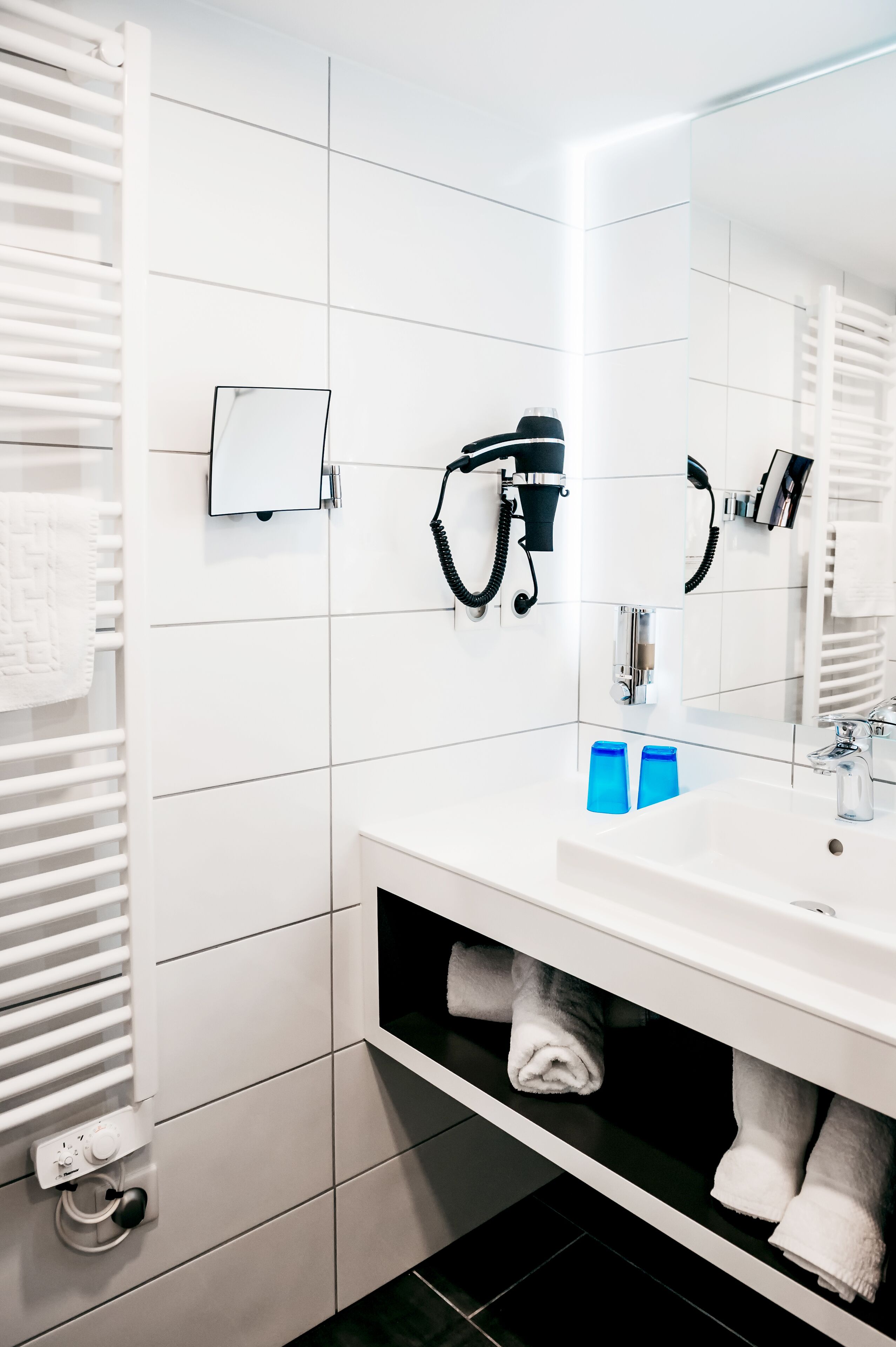 A modern bathroom with a white sink, a mirror, a towel rack, and a hairdryer.