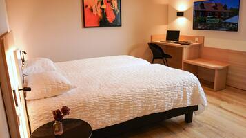 A hotel room with a bed, a desk, a chair, a TV, and a vase with flowers.
