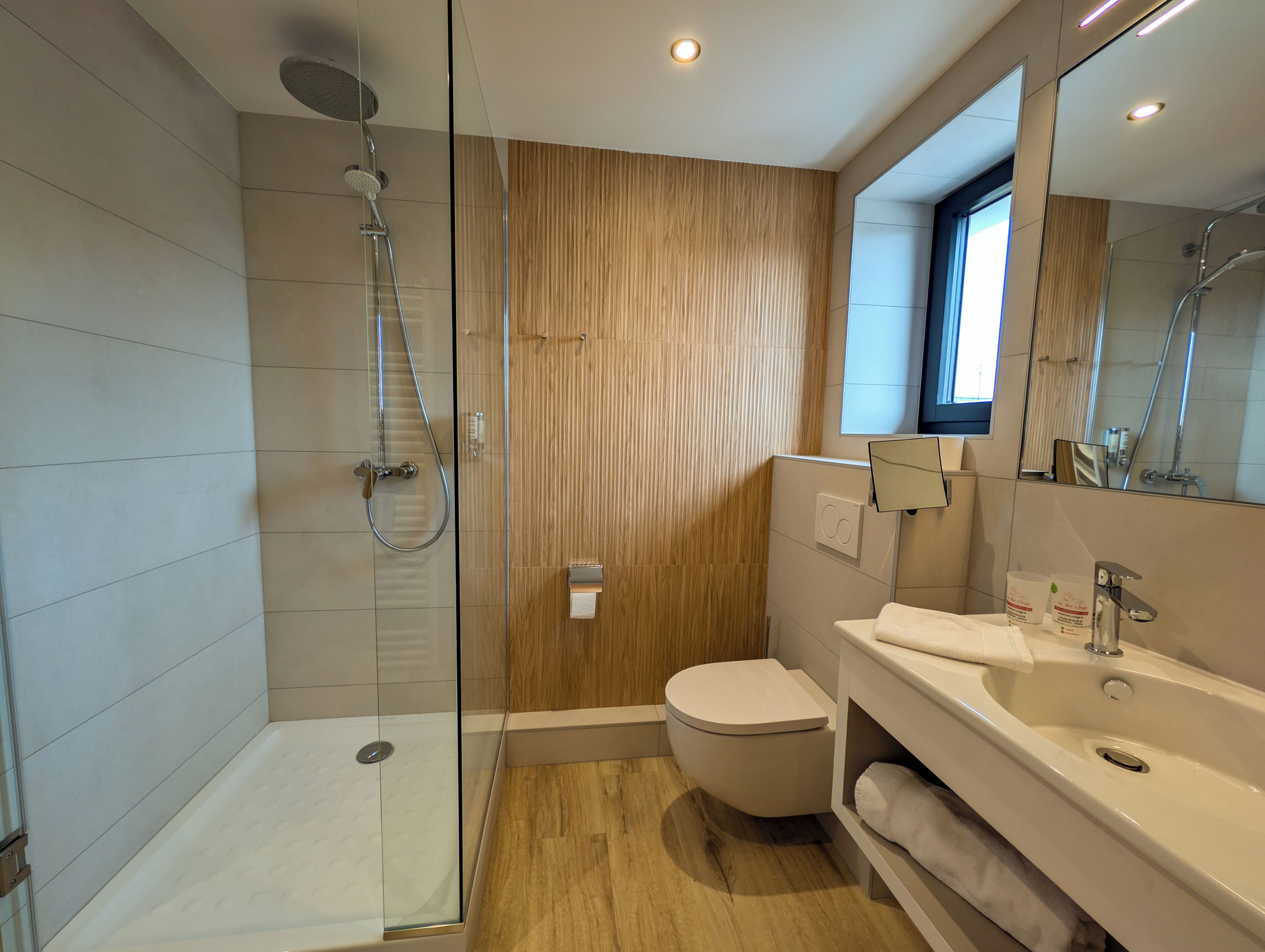 Un bagno moderno con cabina doccia in vetro, parete rivestita in legno, un water e un lavandino con specchio.