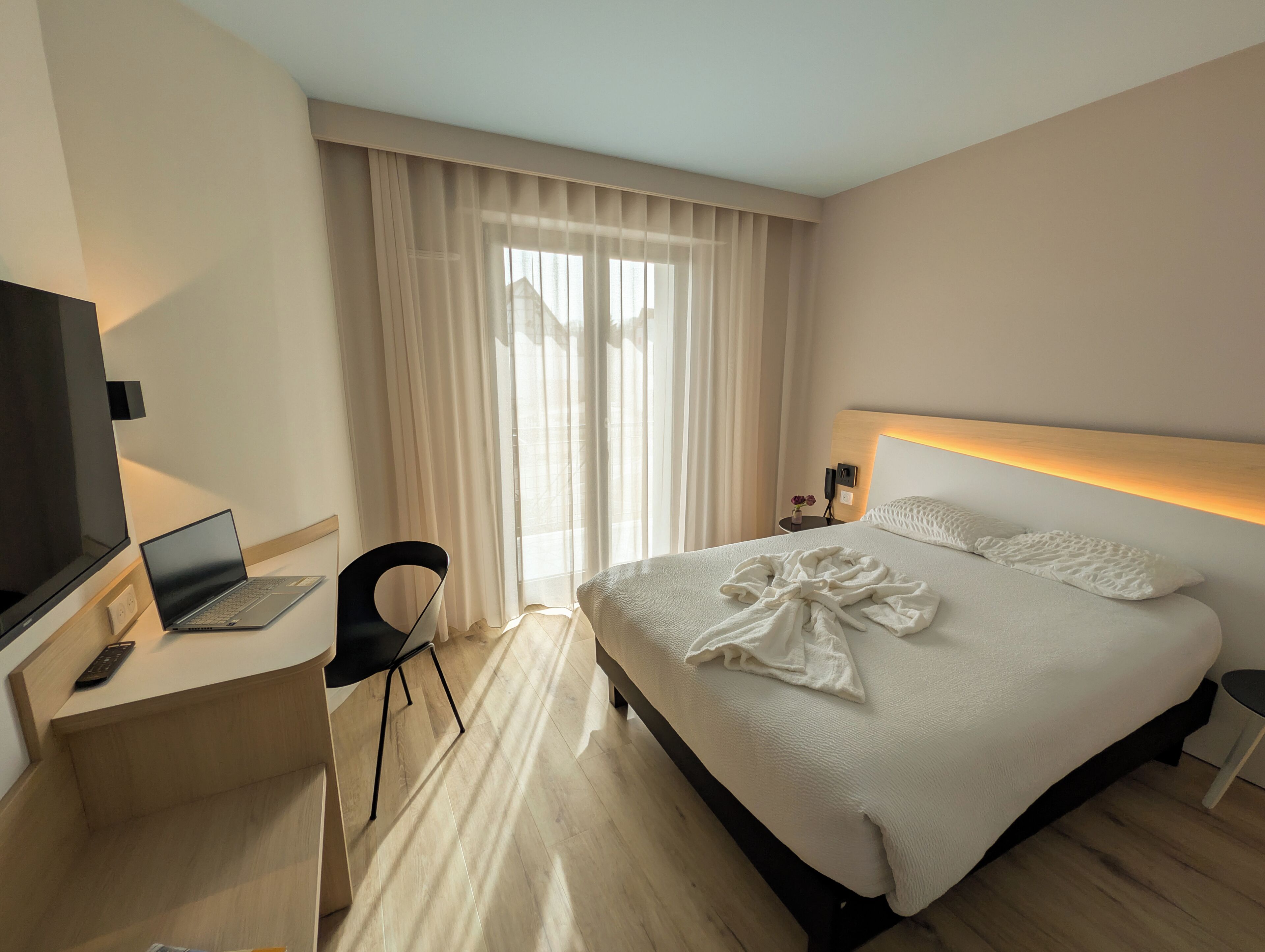 Une chambre d’hôtel comprenant un lit, un bureau avec un ordinateur portable, une chaise, une télévision et une table de chevet avec une lampe.