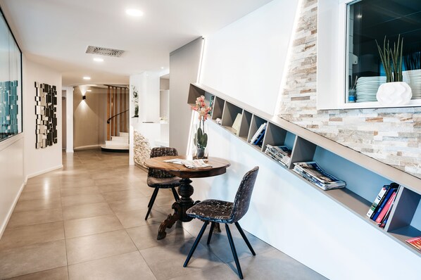 Uma área de jantar moderna com uma mesa redonda, duas cadeiras e uma estante com livros e objetos decorativos.