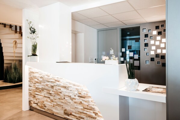Een moderne receptie met een wit receptiebalie, een accentmuur van steen en decoratieve planten.