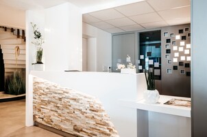 Un área de recepción moderna con un mostrador blanco, una pared decorativa de piedra y plantas ornamentales.