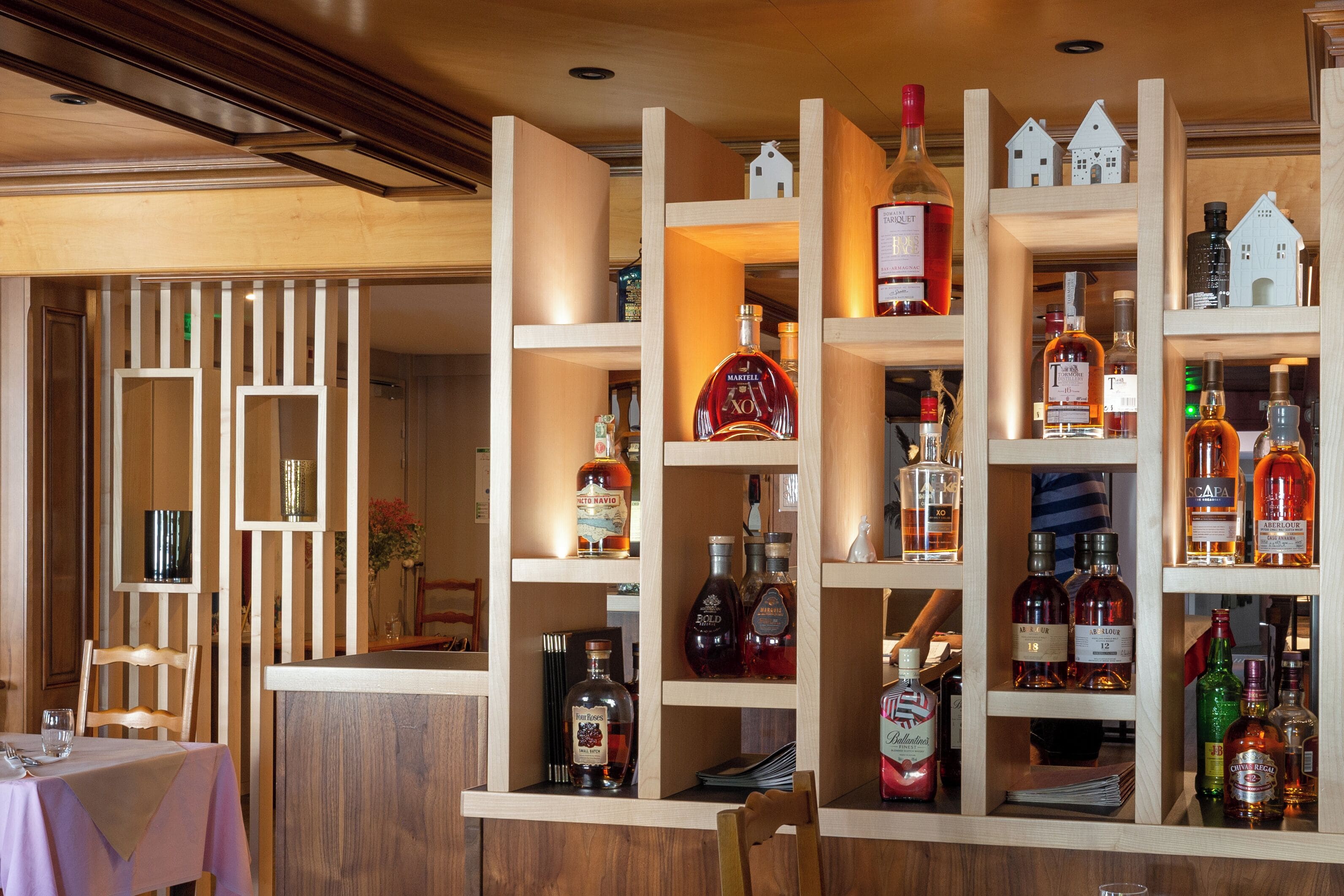 A bar area with wooden shelves displaying various liquor bottles.