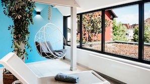 A modern room with a white lounge chair, a hanging chair, and a view of a garden through large windows. - Logis Hôtel Au Lion Rouge (Bartenheim)