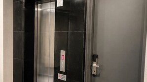Un ascenseur moderne avec une finition métallique, une porte dotée d’une poignée et une petite poubelle agrémentée d’une plante verte.