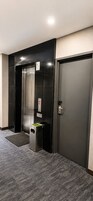 Un ascensor moderno con detalles metálicos, una puerta con manija y un pequeño bote de basura con una planta verde.