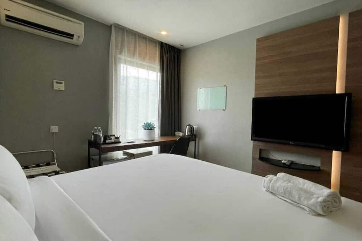 Una habitación de hotel con cama, escritorio, televisor y aire acondicionado.