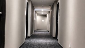 Un long couloir étroit, typique des hôtels, avec un revêtement de sol en moquette et des luminaires encastrés.