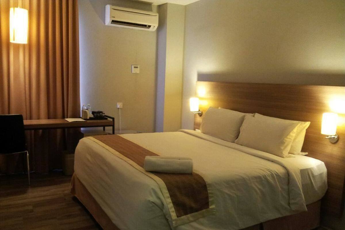 Una habitación de hotel con cama, lámparas de noche, un escritorio y un equipo de aire acondicionado.