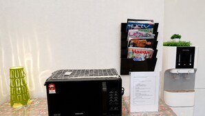 Un coin cuisine équipé d’un four à micro-ondes, d’une machine à café, d’un distributeur d’eau, d’un porte-revues et d’une plante décorative.