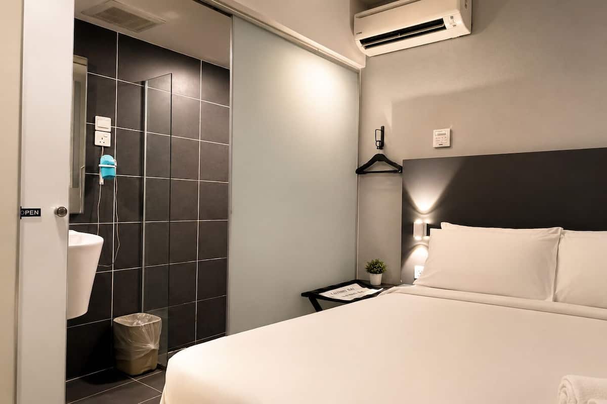 Habitación de hotel con cama, mesita de noche, aire acondicionado instalado en la pared, luz empotrada y una pequeña planta en maceta.