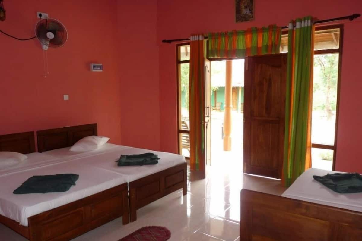Quarto com duas camas de madeira, um ventilador e vista para o exterior por uma porta.