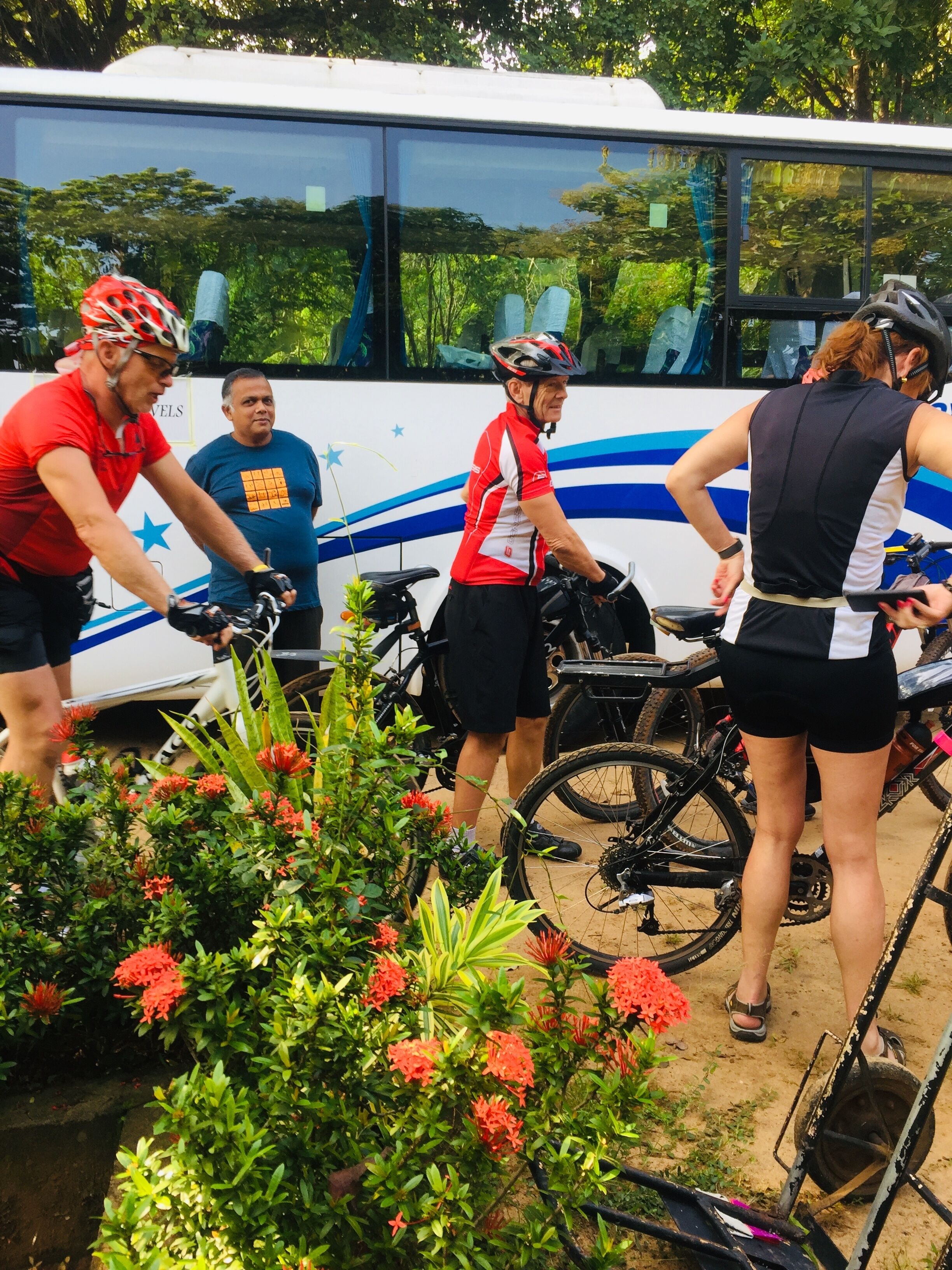 Un grupo de personas cerca de un autobús y bicicletas en un jardín con flores rojas.
