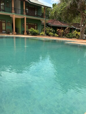 A clear swimming pool with a building in the background. - Melrose Villas (Sigiriya)
