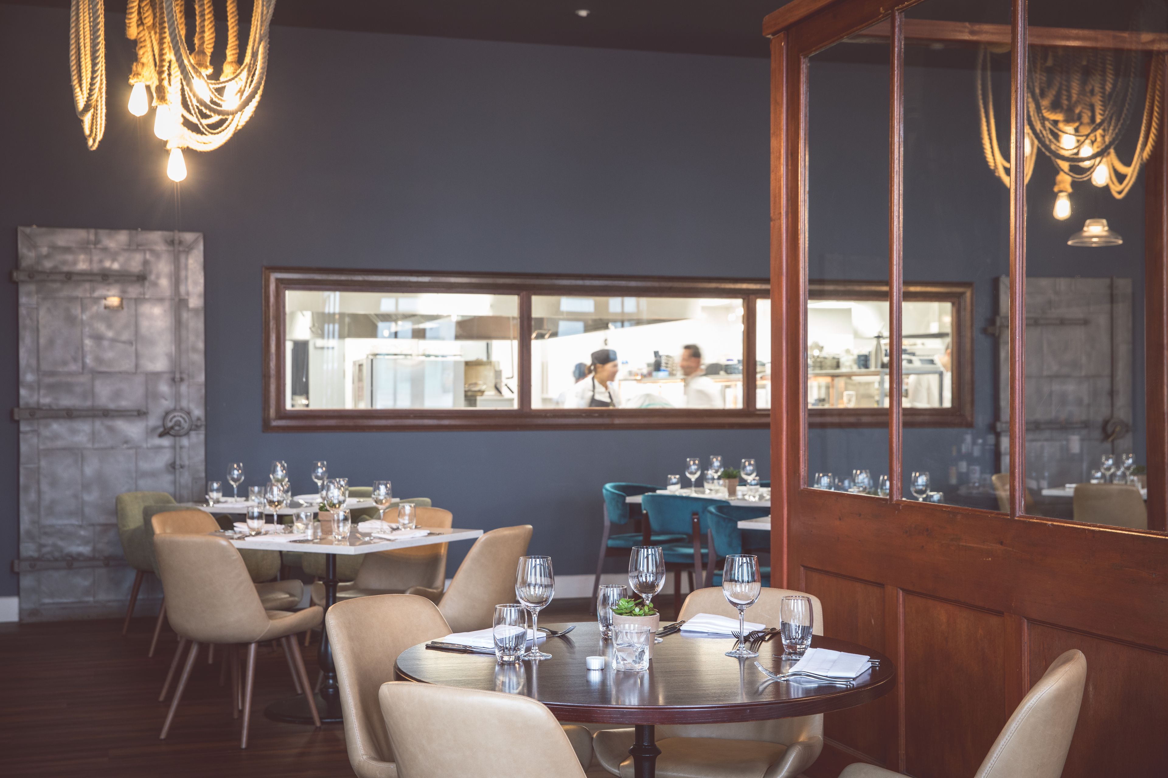 Ein Restaurant mit runden Tischen, einer Steinsäule und einem großen Fenster mit Blick zur Küche.