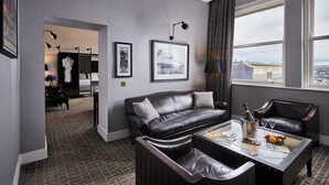 Une chambre d’hôtel moderne avec un canapé en cuir, une table basse en verre et une vue sur la ville grâce à de grandes fenêtres.