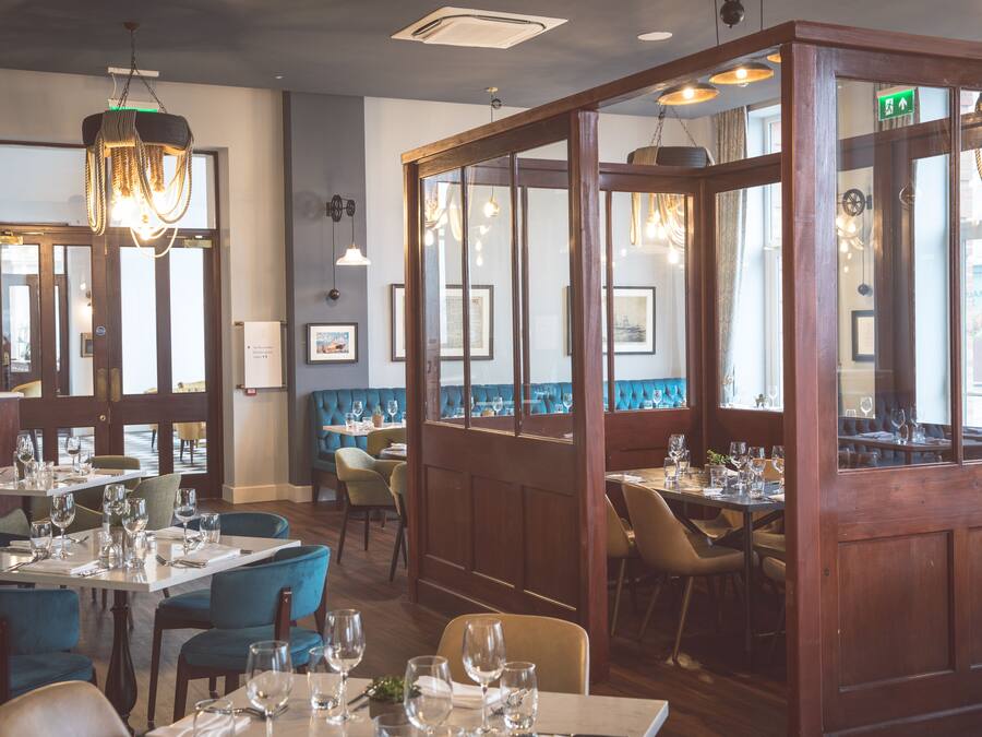 A restaurant interior with wooden paneling, blue upholstered chairs, and tables set for dining.
