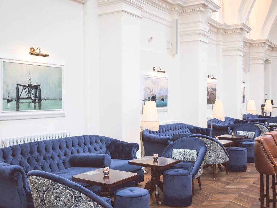 A luxurious hotel lobby with plush blue sofas, a wooden coffee table, and a leather armchair.